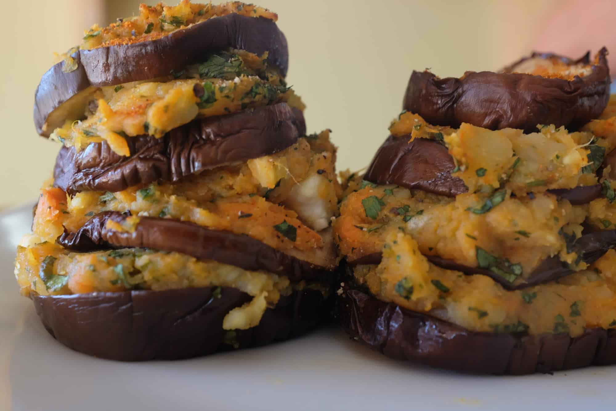 A close up view of roasted eggplant stacks with sweet potatoes, herbs and feta, displaying the layers, by Foodjoya